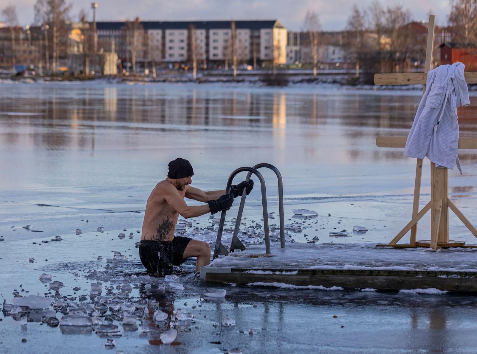 A cold-water plunger climbing out of a frozen lake at dawn